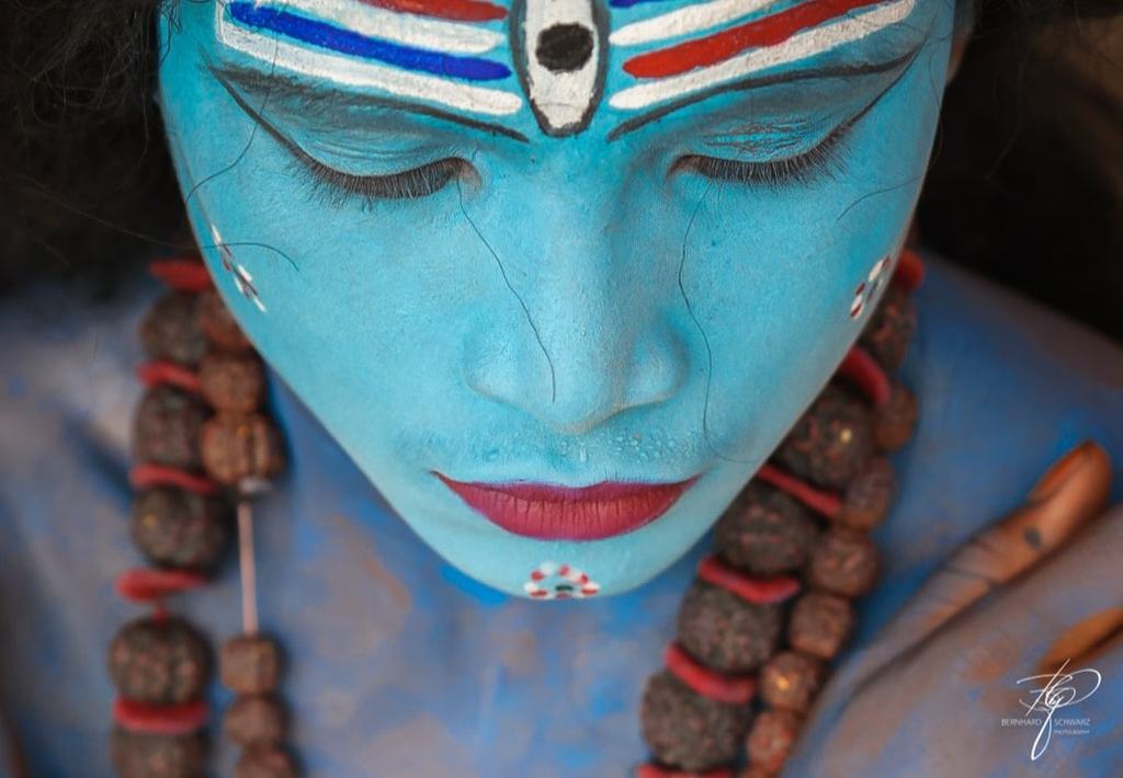 Blau bemaltes Gesicht mit weiß-roten Streifen auf der Stirn, Rudraksha-Ketten um den Hals, die Augen geschlossen