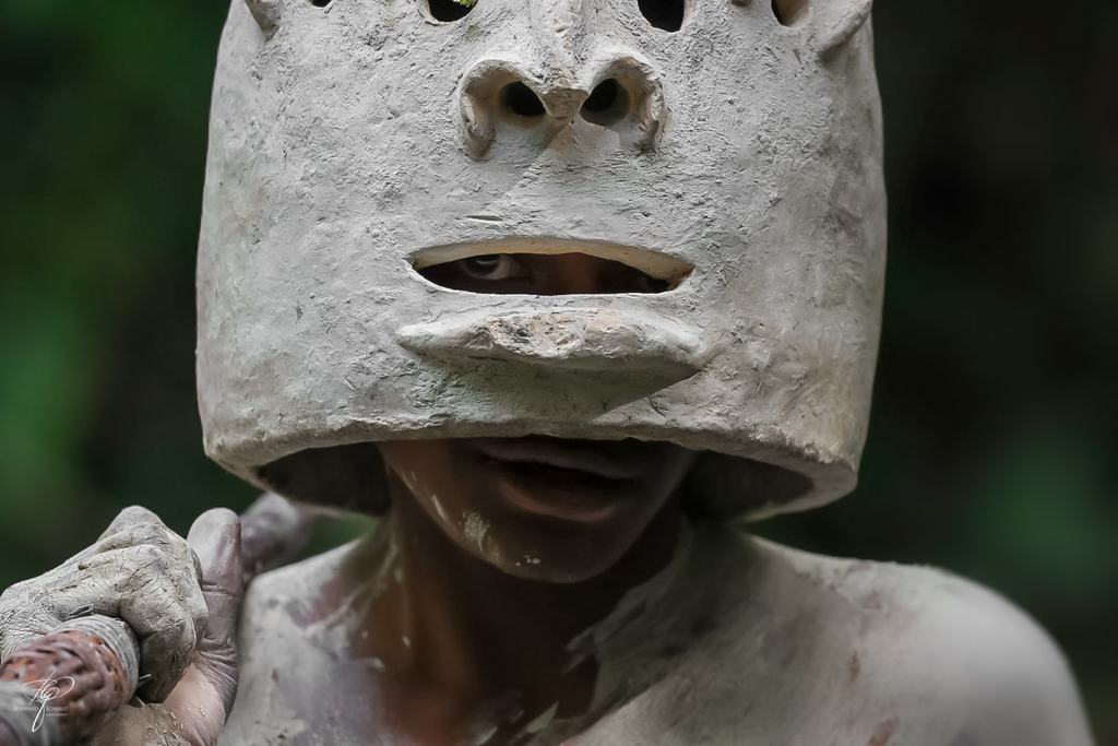 Person mit einer Maske aus Lehm, der Körper hell eingestäubt