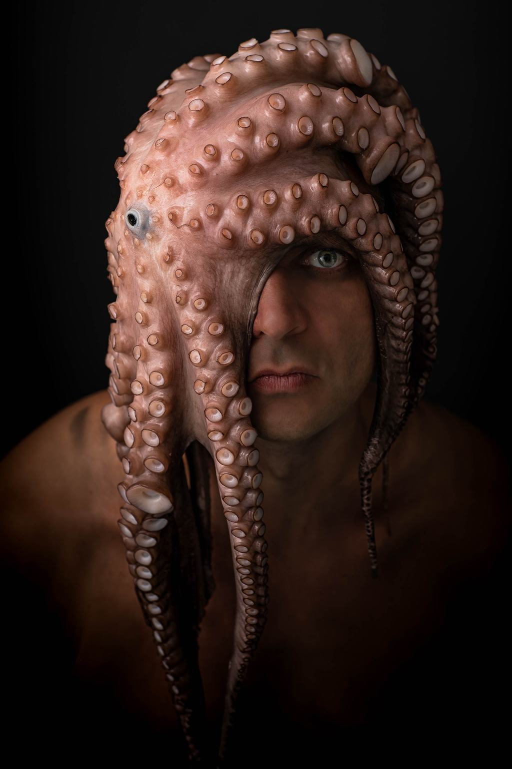Bernhard Schwarz mit nackten Schultern vor schwarzem Grund, über Kopf und Stirn liegt ein Oktopus, dessen Arme über die linke Gesichtshälfte fallen