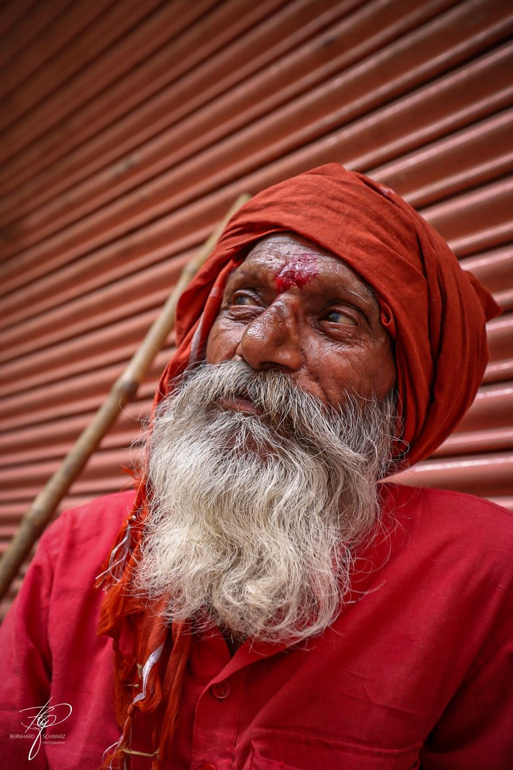 Sadhu mit rotem Turban und langem weißen Bart vor einem roten Rolltor
