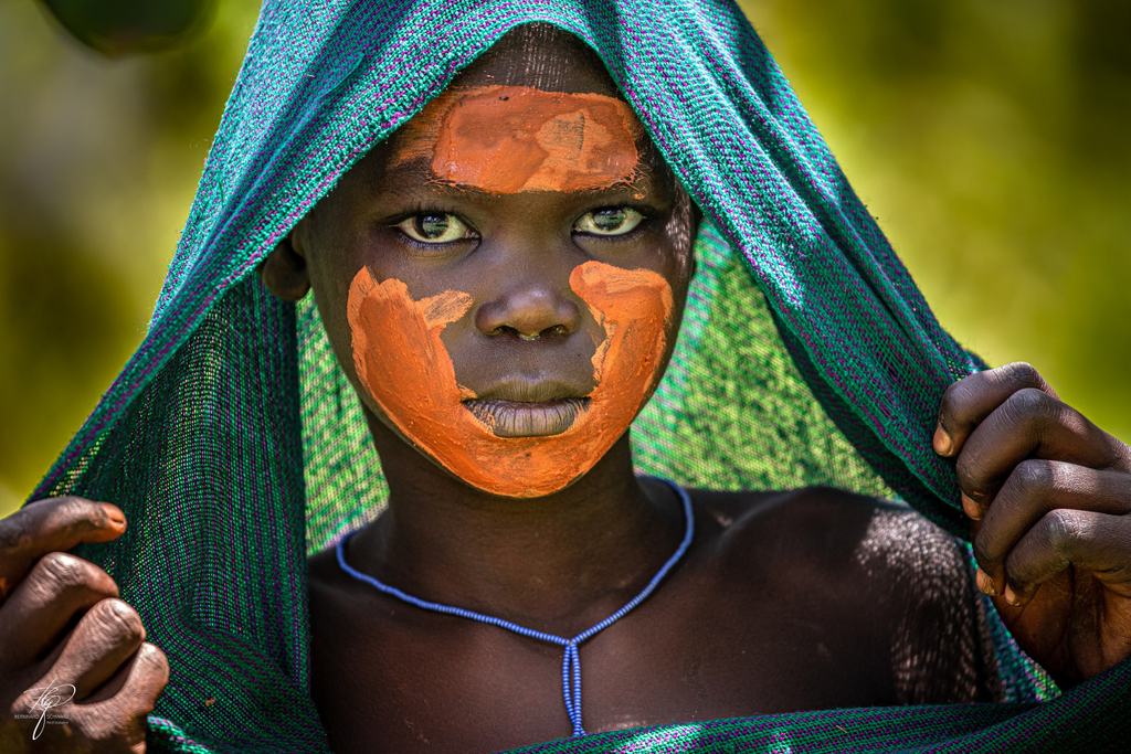 Kind mit orange bemaltem Gesicht hält ein grünes Tuch über den Kopf