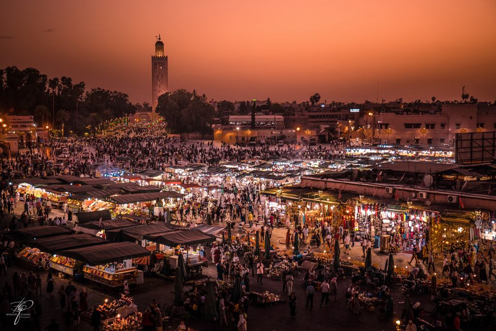 Ein Marktplatz bei Abenddämmerung von oben, die Lichter der Stände, dahinter ein Minarett