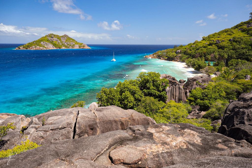 Eine Bucht mit Granitfelsen und türkisem Wasser, ein Katamaran ankert davor
