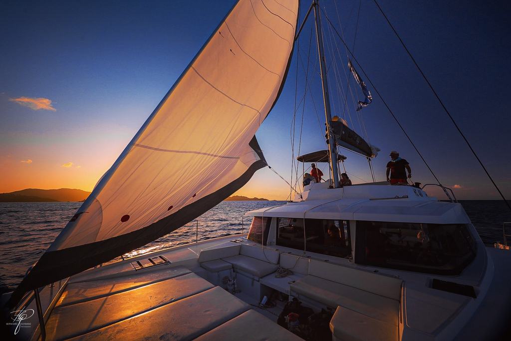 Ein Katamaran unter Segeln im Abendlicht, Menschen an Deck
